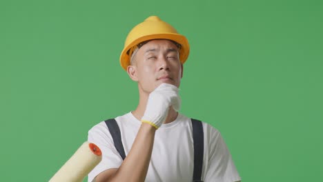 close up of asian man painter wearing safety helmet thinking and looking around then raising his index finger while standing in the green screen background studio