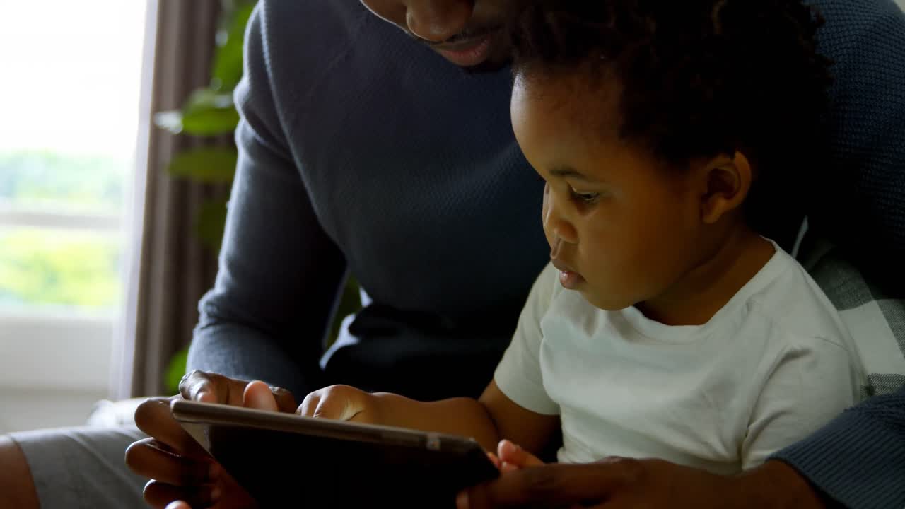 Close-up of young black father and son using digital tablet in a comfortable home 4k