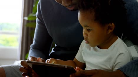 Primer-Plano-De-Un-Joven-Padre-Negro-Y-Su-Hijo-Usando-Una-Tableta-Digital-En-Una-Cómoda-Casa-4k