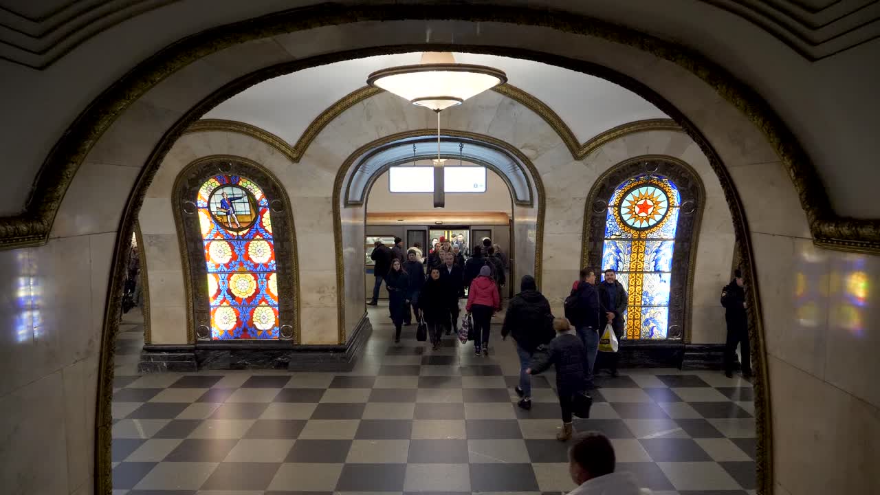 As the train arrives at the Moscow metro station, commuters swiftly exit and navigate the bustling terminal, with vibrant stained glass windows illuminating the space.