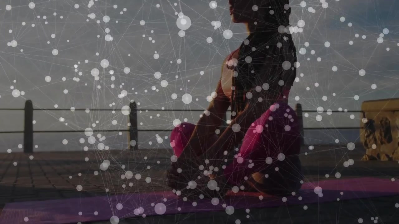 Istruttore di fitness che pratica la respirazione consapevole su un tappetino rosa di fronte all'orizzonte di un mare calmo all'alba.