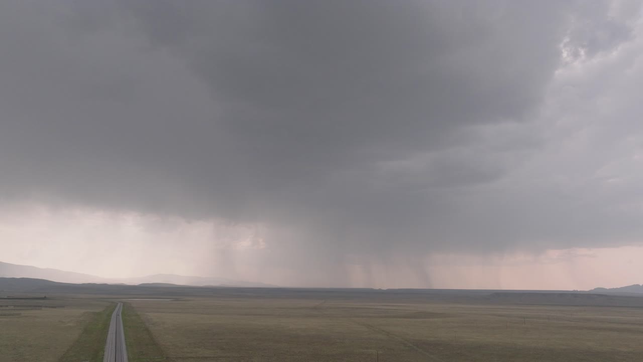 una distante tormenta se avecina sobre un vasto paisaje abierto con la lluvia cayendo en la distancia