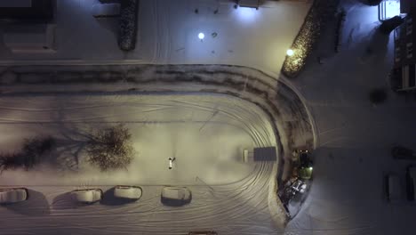 top down view of the winter service, snowplow removing snow from the street, cold winter evening, snow covered cars and streets at night, dark with city lights