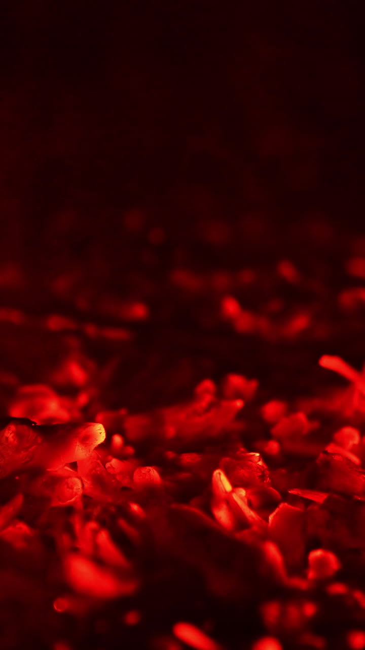 Glowing pieces of charcoal sparkling beautifully. Little flames of fire break out again. Close up. Vertical video