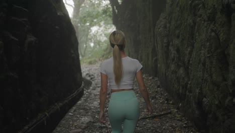 fit athletic blond woman walking through misty canyon with levada waterway, behind shot