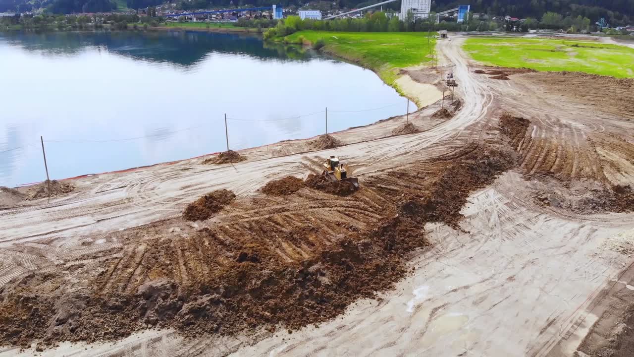 Bulldozer pushing sand along Velenje Lake shore. Aerial forward