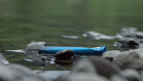 trash floating on rocky rivershore at daytime