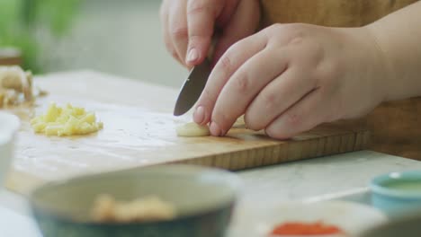 Mujer-Cortando-Ajo-Sobre-Tabla-De-Madera-En-La-Cocina