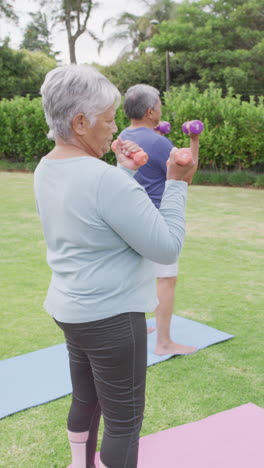 vertical video of happy senior biracial couple exercising in garden