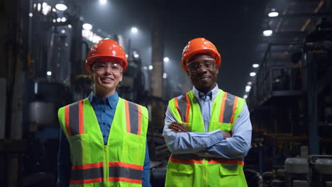 multiethnic engineers smiling camera wearing safety uniform at huge factory.