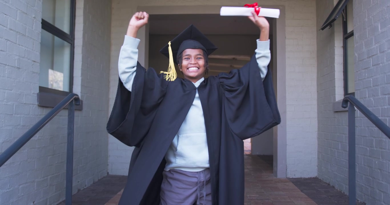African teen male graduate gowned celebrating holding rolled diploma crouching then rising on steps
