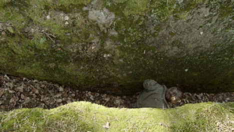 Young-boy-passing-in-between-two-giant-boulders-adventuring-through-forest---Overhead-wide-static-shot