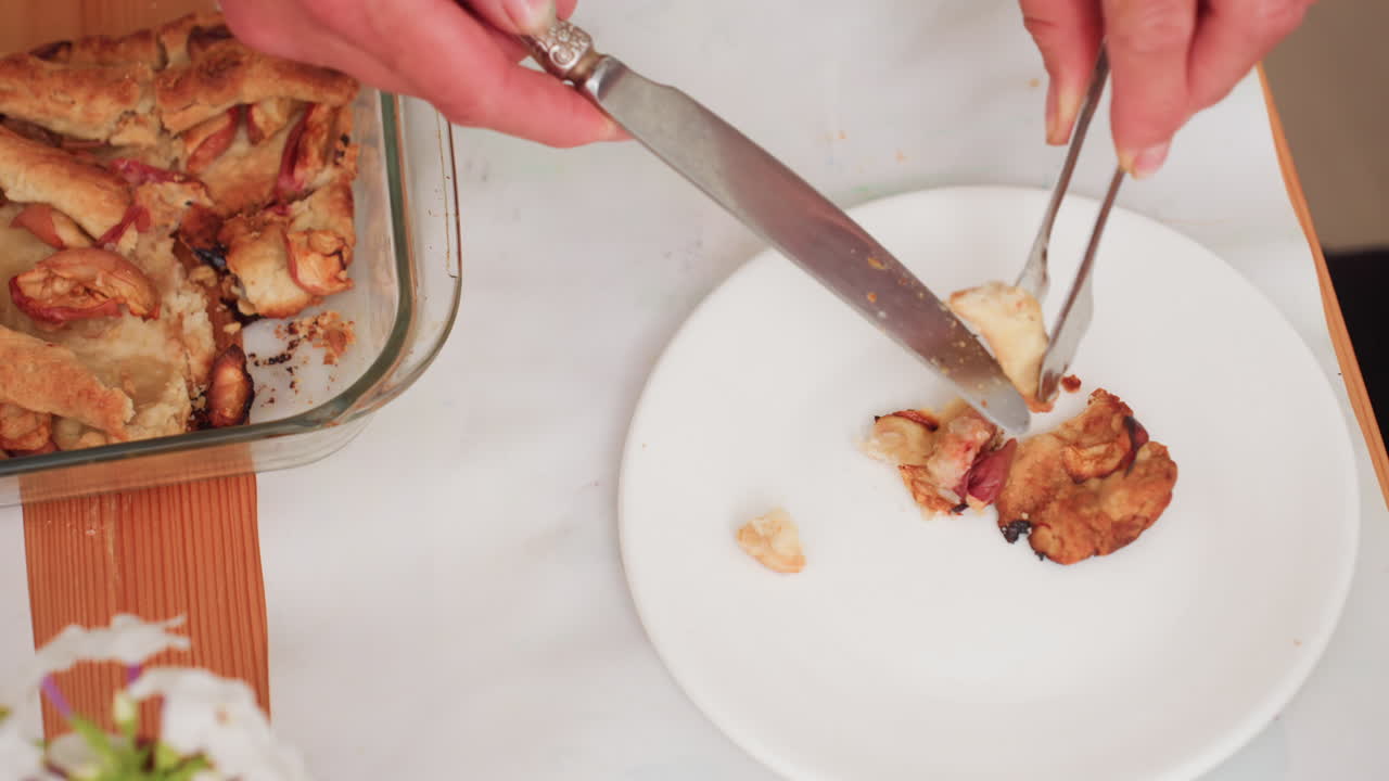 주방에서 요리사가 집게로 음식을 담아 따뜻한 사과 파이 조각을 테이블 위의 유리 베이킹 접시 옆 흰 접시에 올리는 모습이에요. 아이들 점심 식사를 위해 디저트를 준비하는 교실 부엌 풍경입니다.