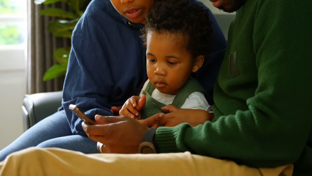 Side view of young black family using mobile phone and sitting on the couch in comfortable home 4k