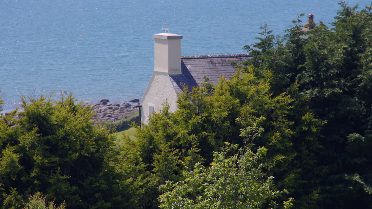 Wide shot of a Gable end of a cottage with trees and wood in foreground at Criccieth