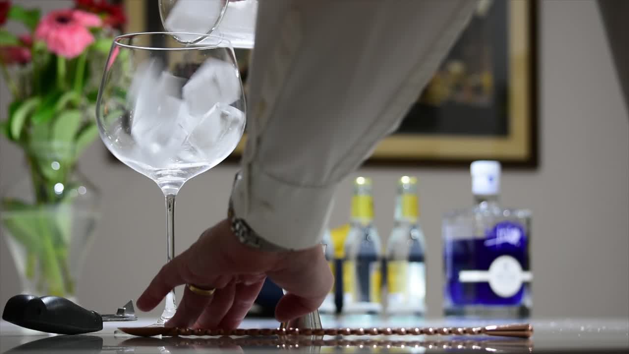 Hælder is i et stort stilket ballonglas som første trin i fremstillingen af en gin og tonic-cocktail