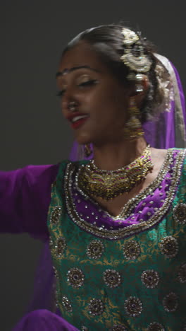 vertical video close up of female kathak dancer performing dance wearing traditional indian dress seated on floor in spotlight 2