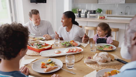 multi-generation mixed race family eating meal around table at home together
