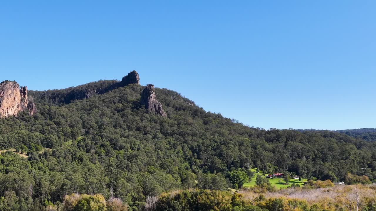 A serene landscape of Nimbin Rocks under clear blue skies, showcasing lush greenery and rocky formations