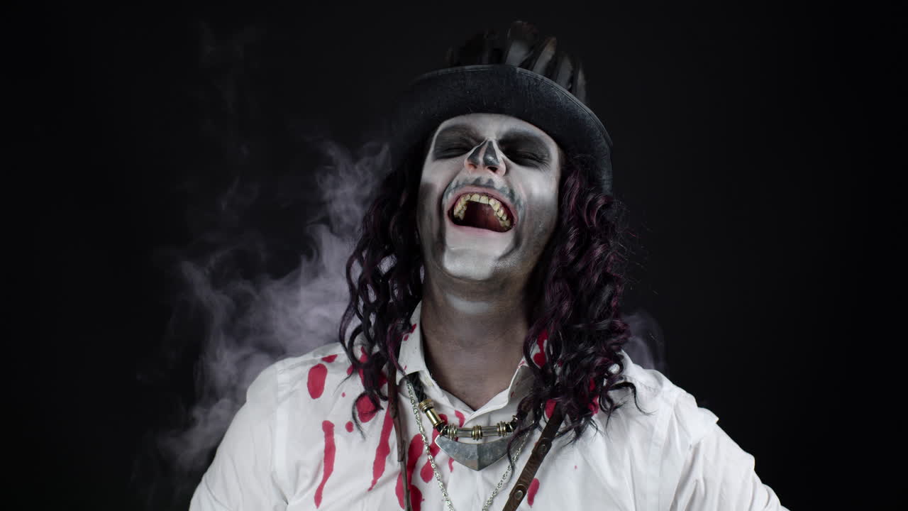 Uomo spaventoso e sorridente con uno scheletro e un costume di Halloween con una camicia insanguinata che guarda e indica la telecamera.
