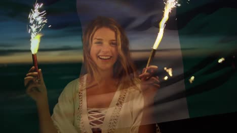 animation of waving flag of nigeria over girl with sparklers having fun on the beach