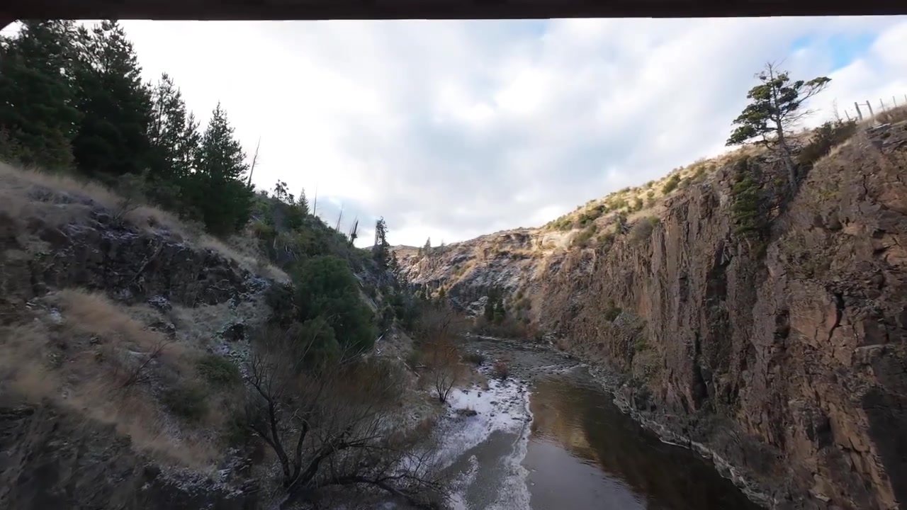 Vuelo aéreo con dron FPV debajo de un puente histórico de celosía metálica sobre el Río Percey en Trevelin, Chubut, Patagonia, Argentina