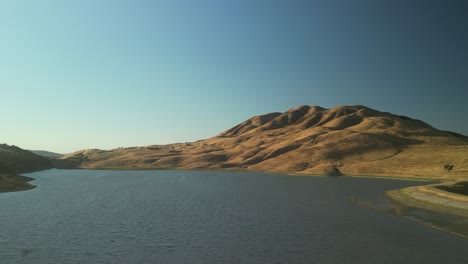 a drone glides over paicines reservoir, unveiling its still waters reflecting the sky, surrounded by quiet farmland in the heart of california.
