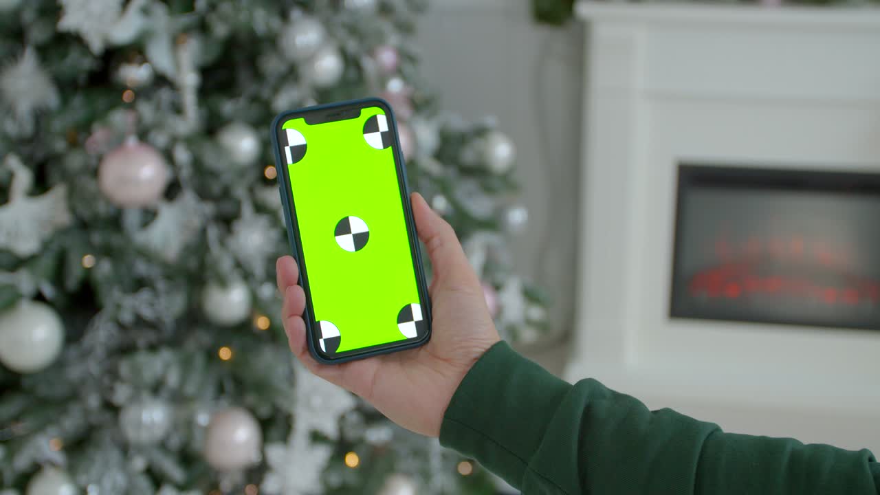hombre sosteniendo una maqueta de teléfono inteligente pantalla verde llave de cromo en la habitación decorada para el año nuevo. primer plano de manos masculinas sosteniendo un teléfono inteligente moderno negro en las manos en el interior de la casa de navidad brillante.