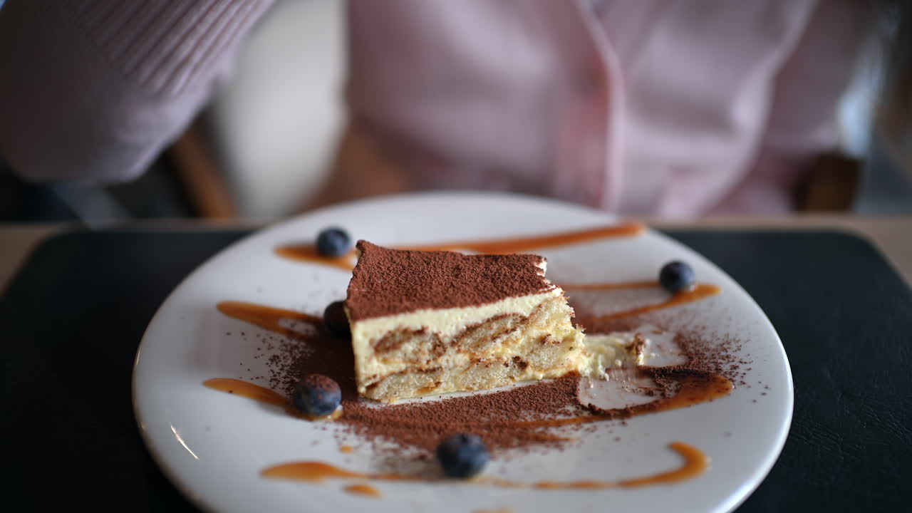 Donna che addenta il tiramisù con la forchetta, su un piatto con cacao in polvere e frutti di bosco.