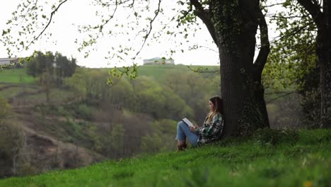 turista con libro descansando en el césped entre los árboles y la montaña