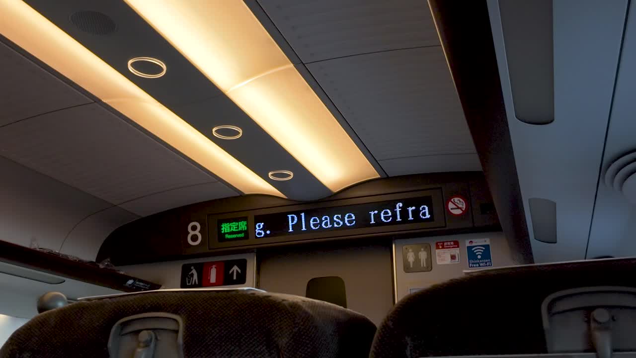 Modern Japanese train displays station information in local language. Shows interior design with soft lighting.