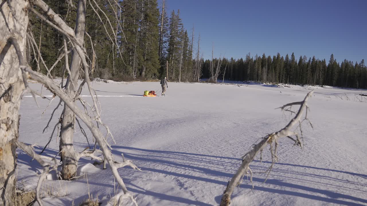Uomo che trascina una slitta da spedizione sulla neve piena di attrezzatura da campeggio attraverso la natura