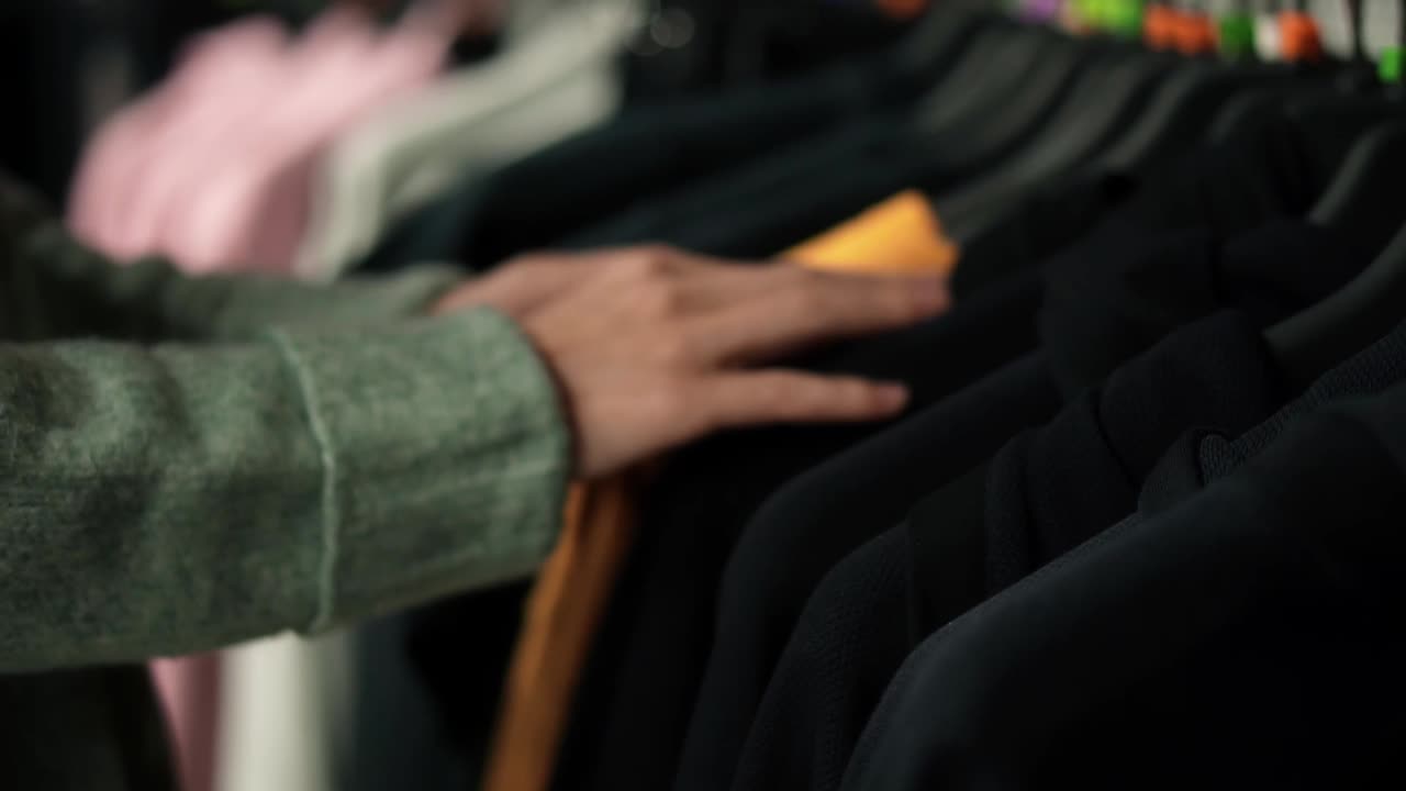 Unrecognizable woman choosing clothes from rack in clothing store