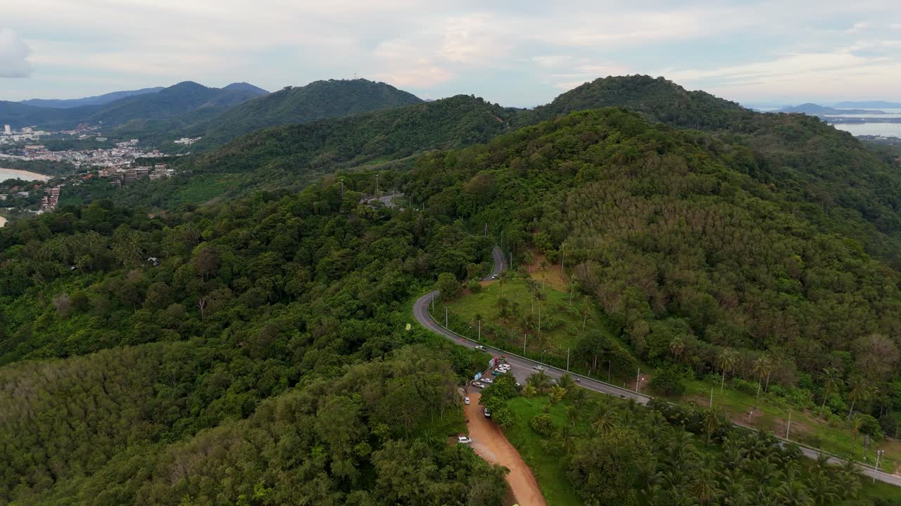 vuelo de avión no tripulado a una carretera con coches en movimiento en el bosque tropical con palmeras verdes y árboles en 4k en las islas de phuket, en el fondo son las montañas, la ciudad y el océano con pequeñas islas