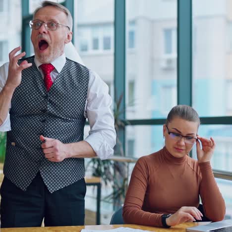 secretary and her mature boss in office. senior businessman puts document on the desk angrily and feels ashamed. slow motion.