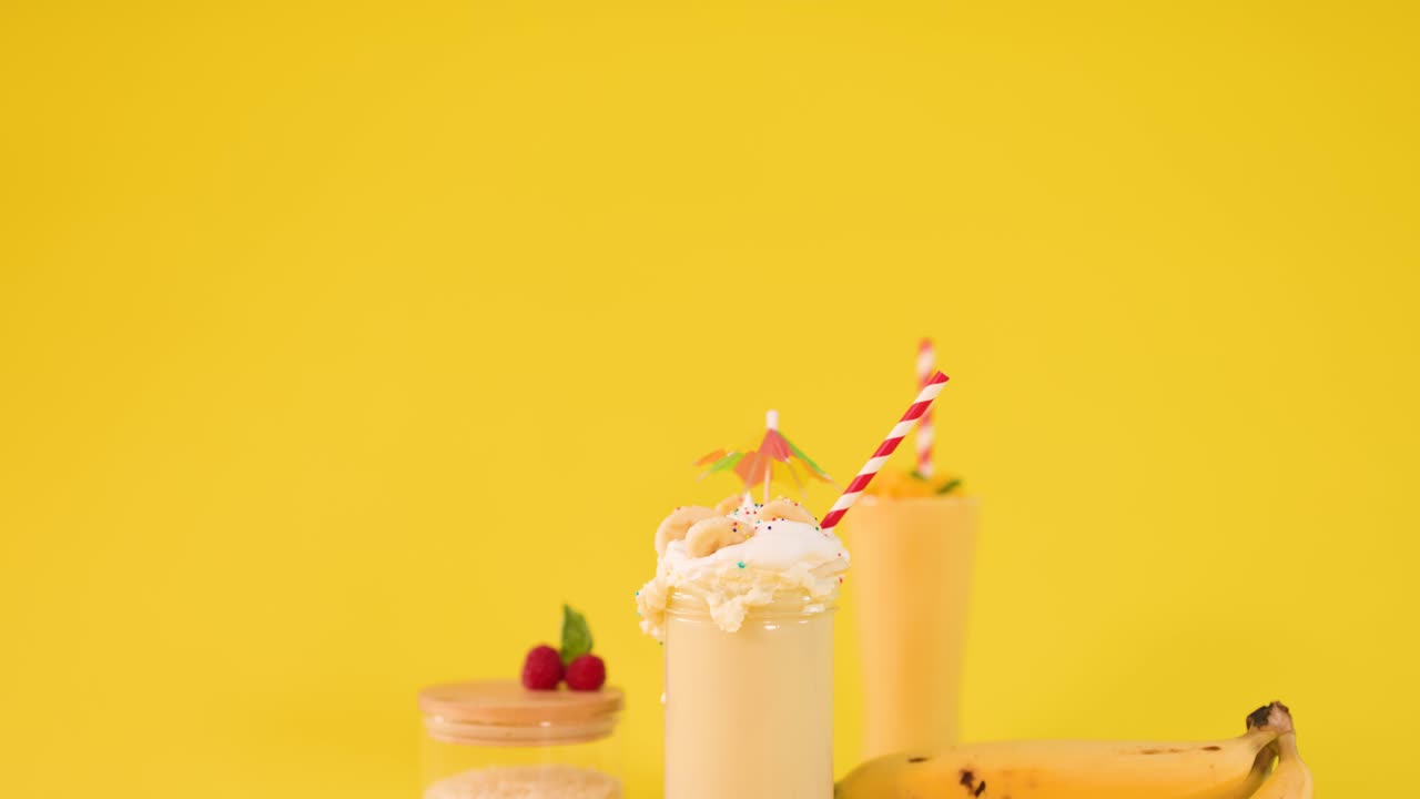 La telecamera si sposta lentamente verso una composizione di frullati alla banana su sfondo giallo con illuminazione da studio vivace
