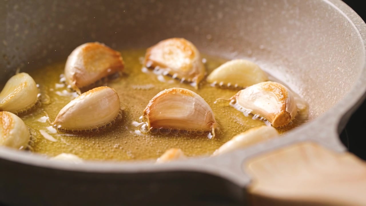 Il calore del fornello fa sfrigolare spicchi d'aglio dimezzati, che si dorano per un sapore dorato in padella con olio.