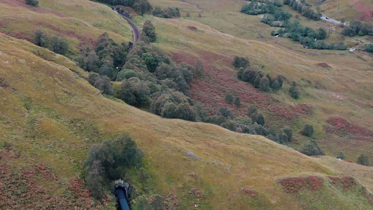 seguimiento aéreo del tren de vapor jacobita que cruza el túnel y serpentea a través de las tierras altas