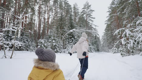 una mujer alegre y su pequeño hijo en un viejo trineo de madera caminan por el bosque en invierno