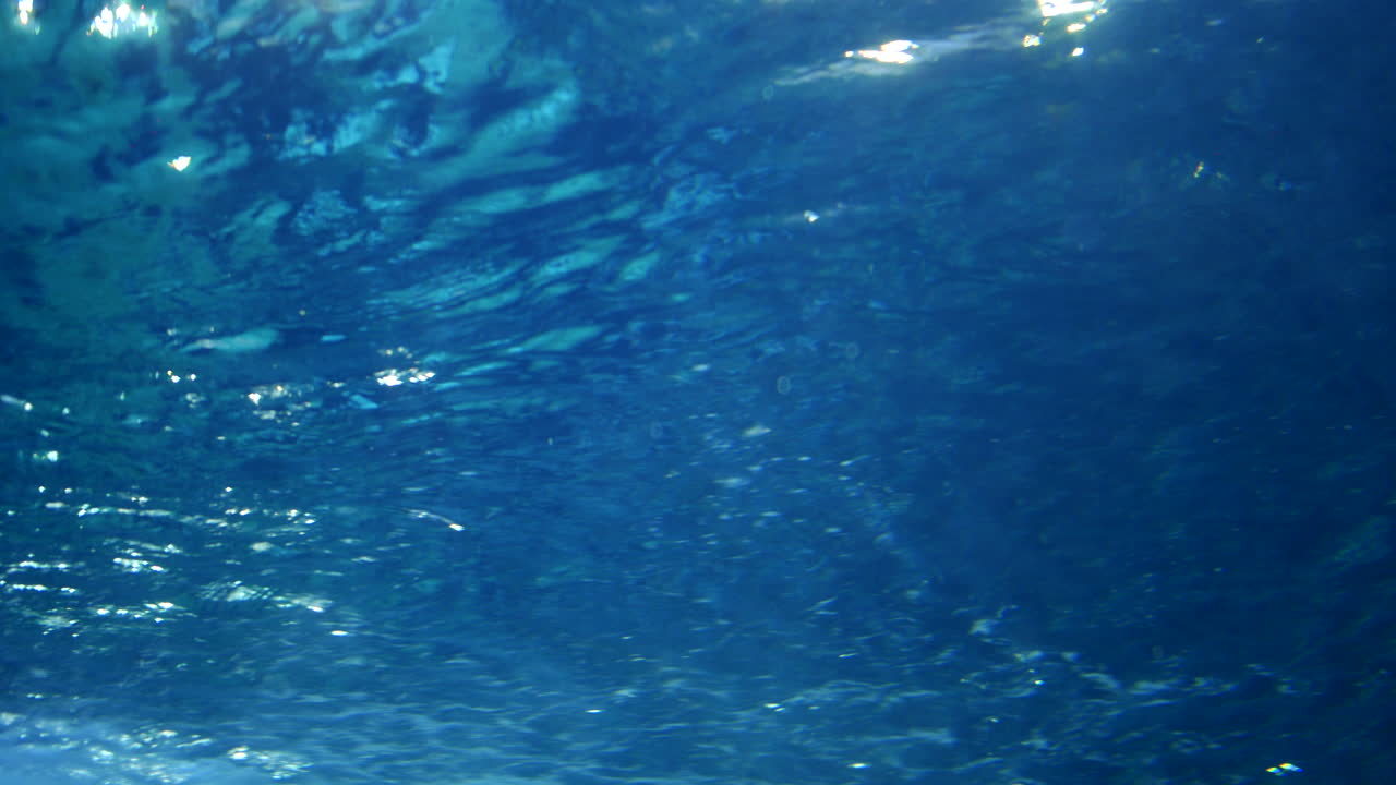 Vista subacquea di increspature di luce solare che si riflettono sulla superficie dell'acqua blu, creando motivi scintillanti sotto le onde. Il flusso pacifico dell'oceano o di una piscina.