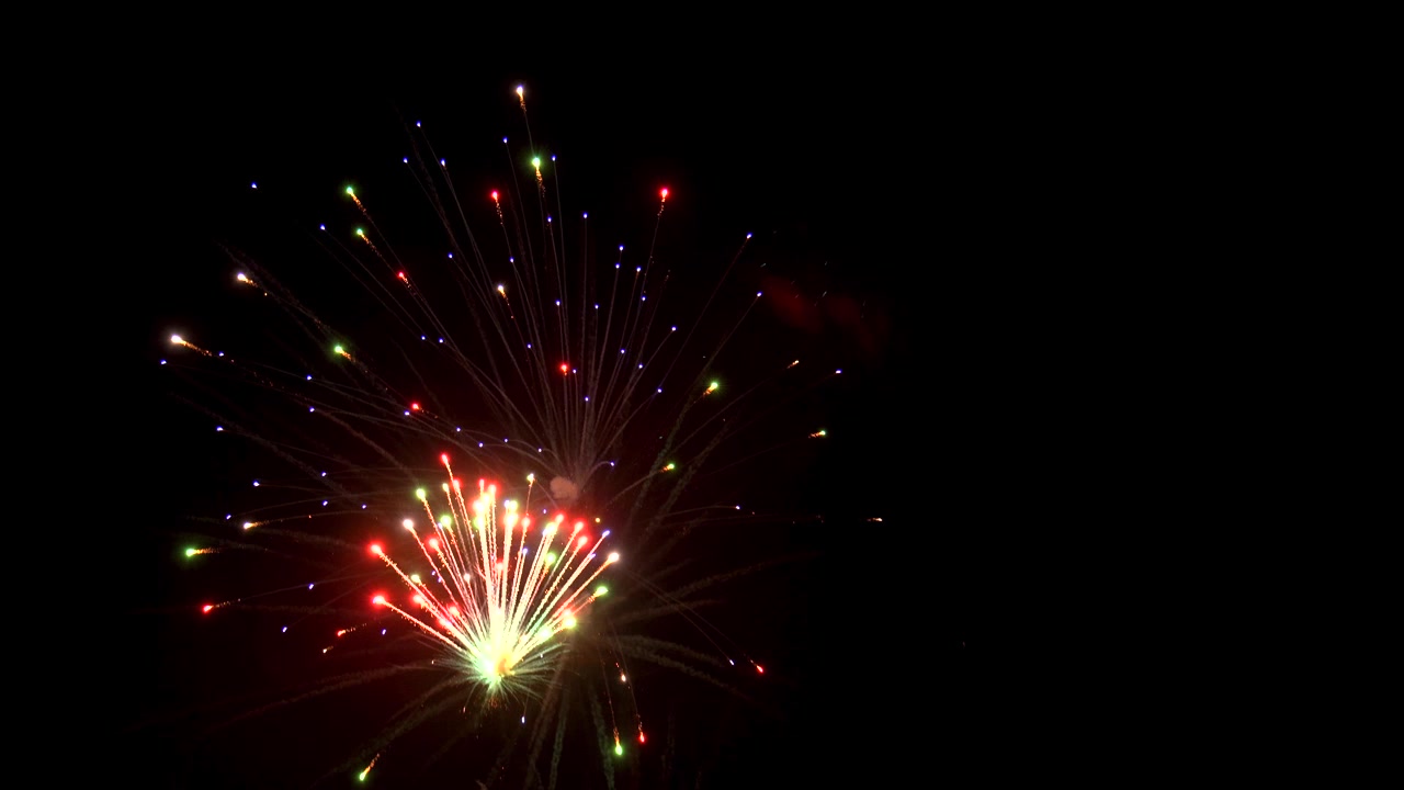 Multiple colors burst from exploding fireworks against black night sky to thrill viewers out of frame