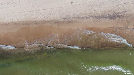 aerial drone footage of baltic sea waves crashing against sandy shoreline in latvia scenic top-down view of coastal landscape on a bright sunny day with natural rhythmic ocean motion