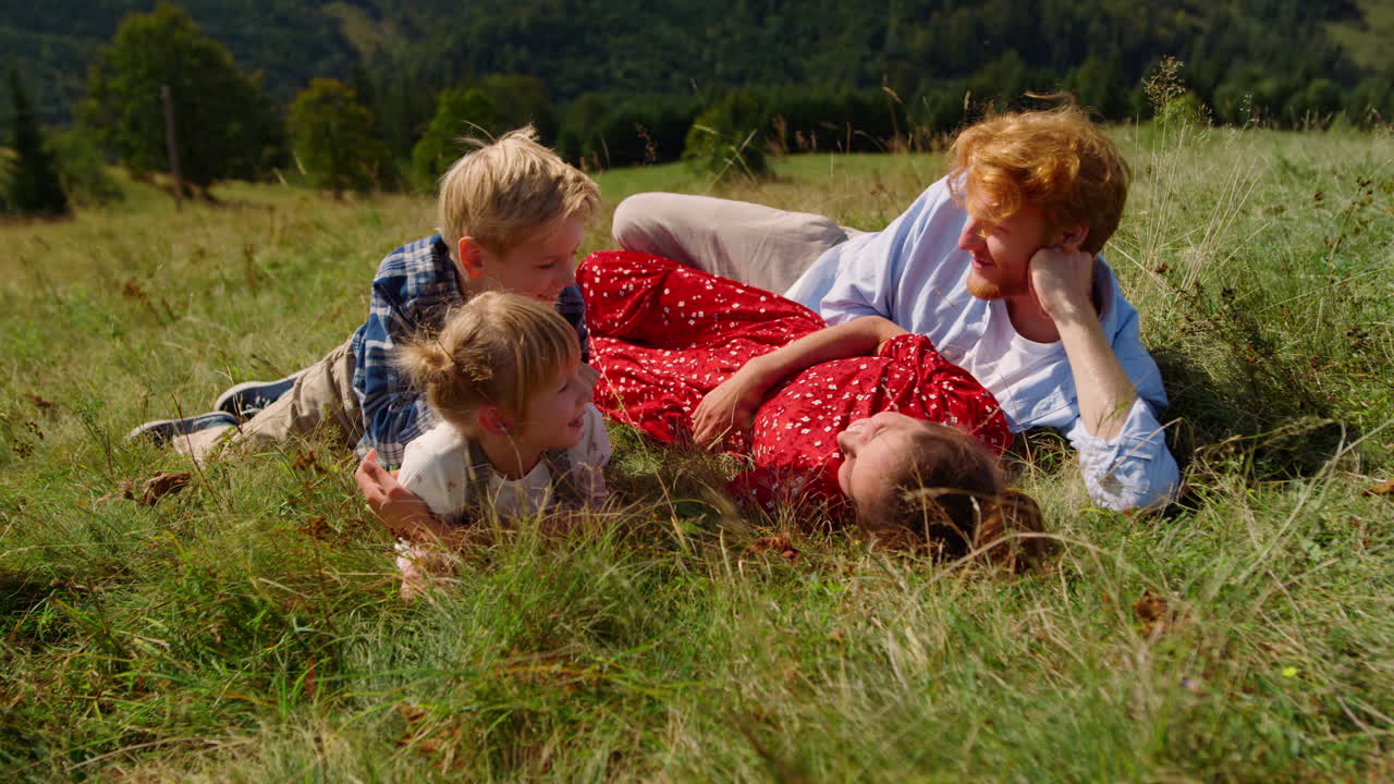 Familien ligger på grønt græs på en smuk skråning. Unge forældre hviler med børnene.