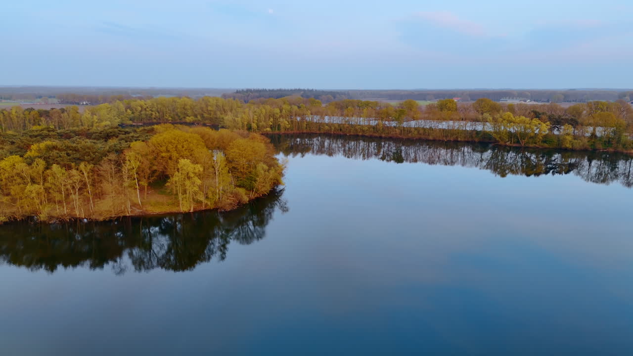 Aerial view of Dutch landscape. A tranquil view of a serene lake surrounded by lush green and yellow trees in the Netherlands during dusk