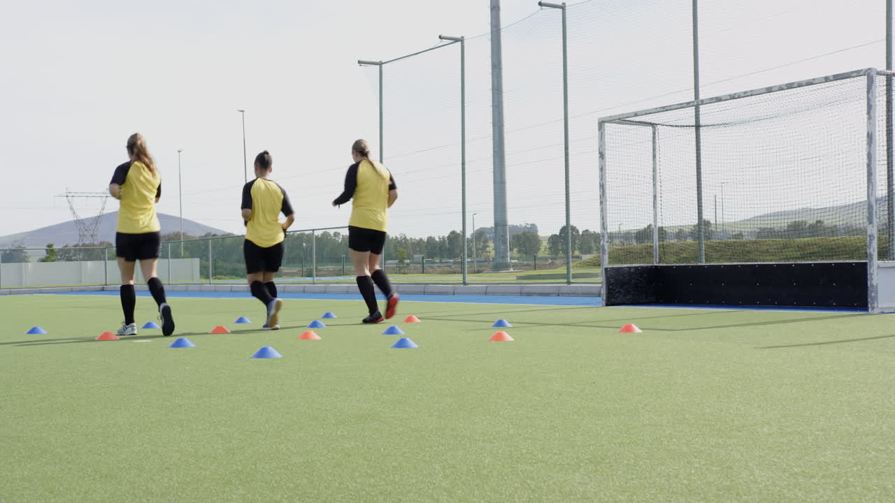 Female hockey players practicing drills on field, focusing on teamwork and skills