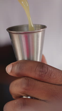 el camarero vierte jugo en un jigger inoxidable en un bar de primer plano. el camarero afroamericano mide los ingredientes líquidos para el cóctel. el hombre negro prepara una bebida exótica
