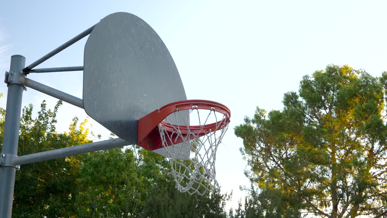 un aro de baloncesto con un tablero de metal, un borde naranja y una red en una cancha del parque al amanecer