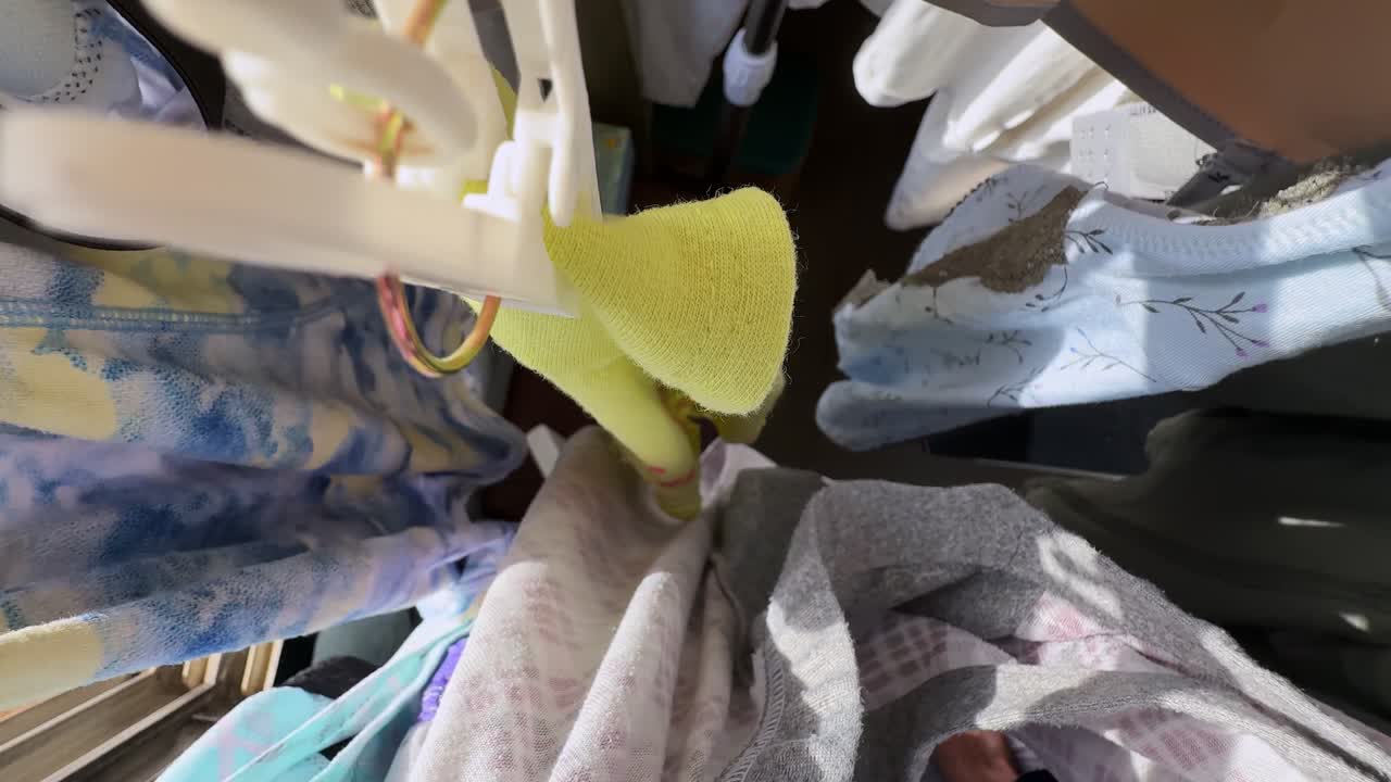 Overhead close-up of mixed laundry, yellow socks, and fabric pieces clipped on a drying rack inside a sunlit apartment, capturing an everyday household washing routine in natural daylight