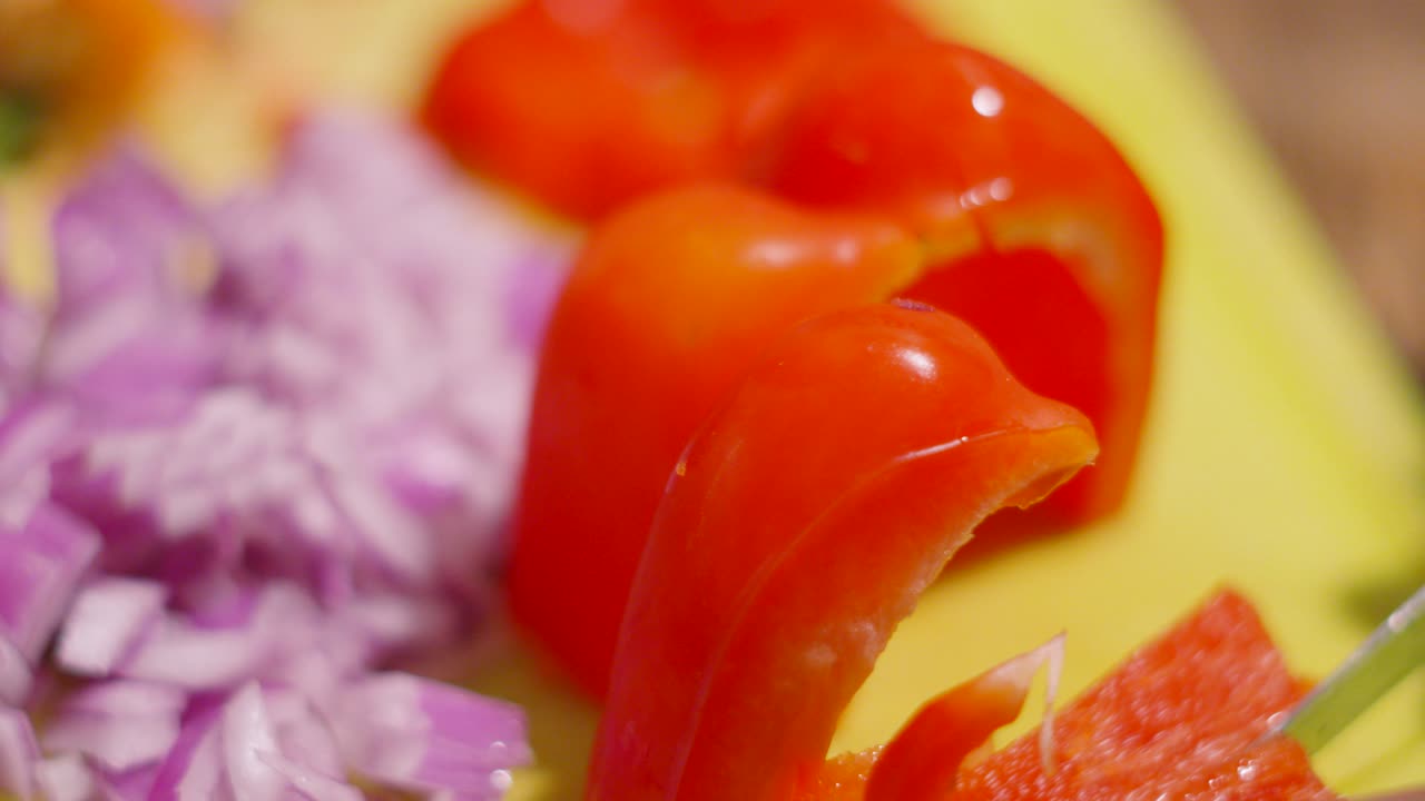 Close Up of Knife Chopping Peppers into Smaller Pieces with Finely Chopped Red Onions in Background
