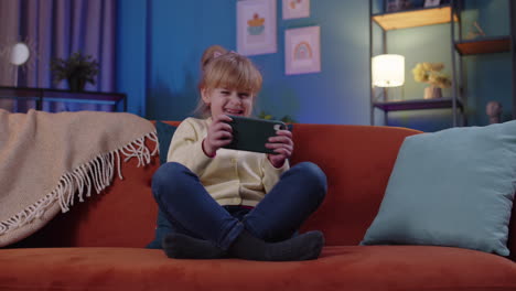 niña preocupada niña niño jugando con entusiasmo a videojuegos de carreras en el teléfono móvil en casa en el sofá